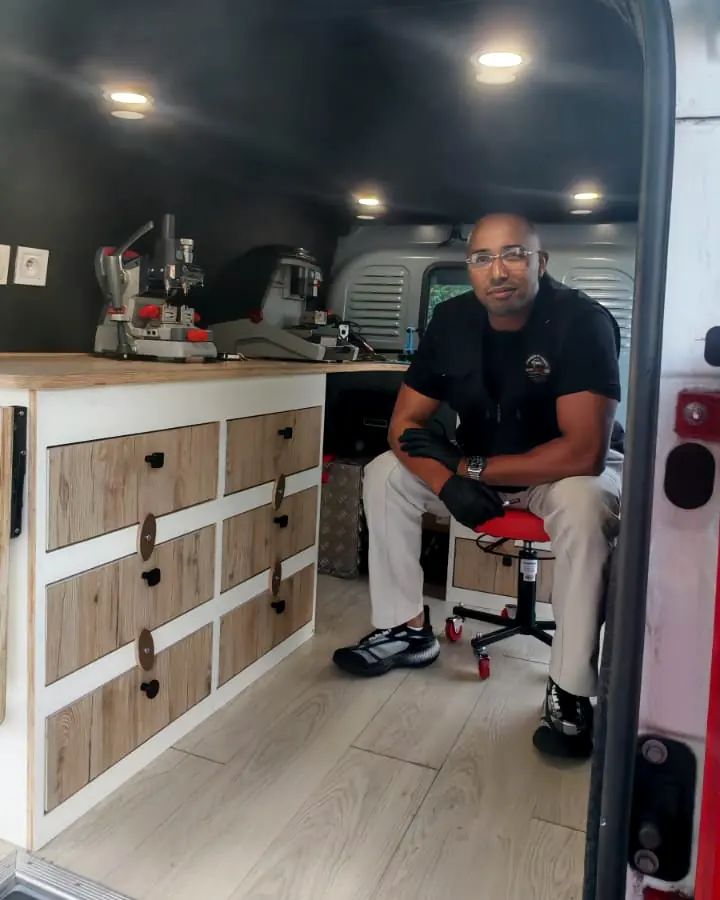Yassine Macid assis dans son camion aménagé, portes arrière ouvertes, devant l’établi et les machines de taille de clés